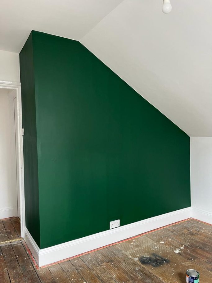 Dark green wall with an angled design, set in a room with wooden flooring.