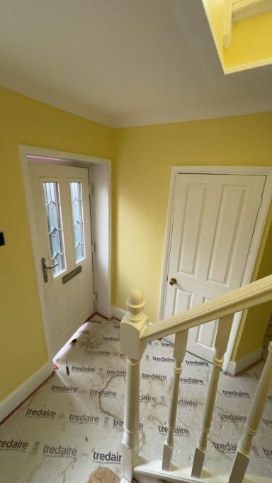 A yellow hallway featuring a door, stairs, and patterned flooring.