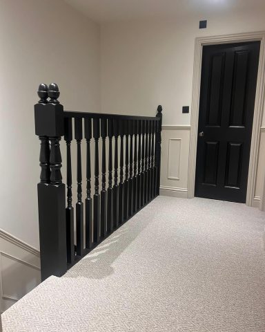Black wooden banister with spindles, carpeted floor, and a closed black door in the background.