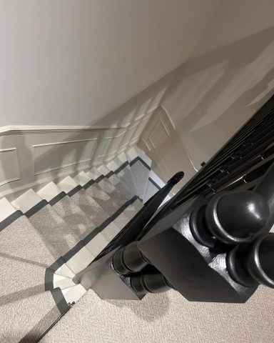 Top-down view of stairs with a black railing and beige carpet.