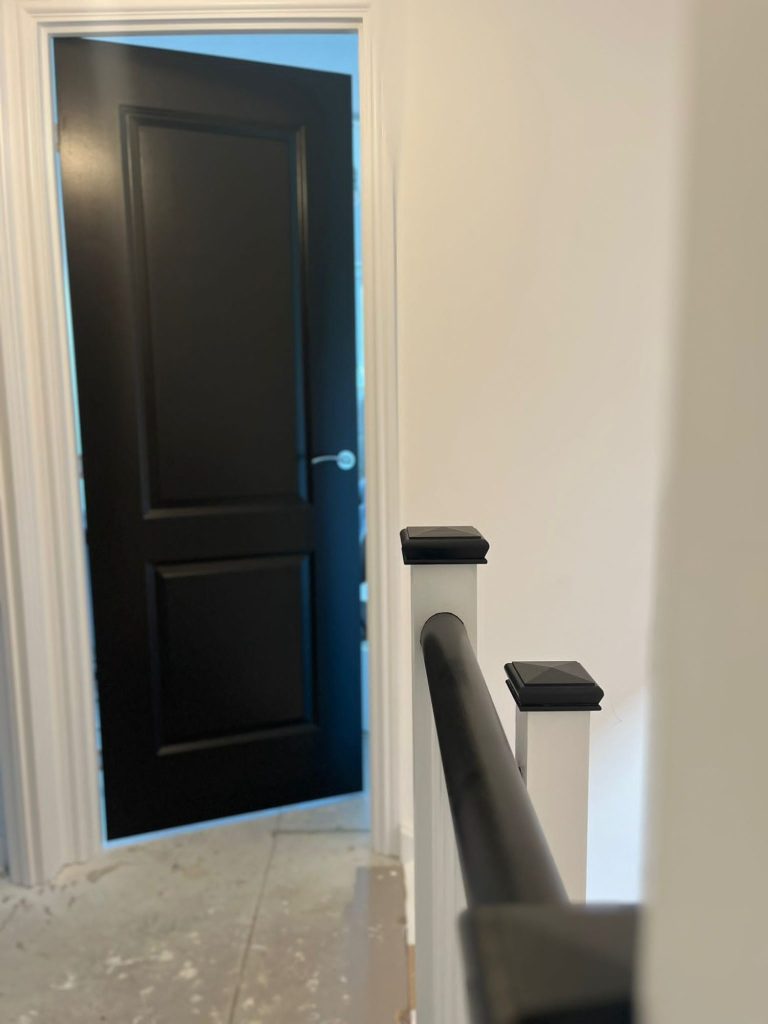 A black painted door slightly ajar at the top of a staircase with a white wall.