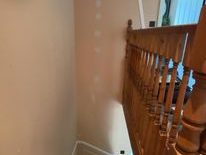 A staircase corner with wooden banister and light reflecting on a plastered wall.